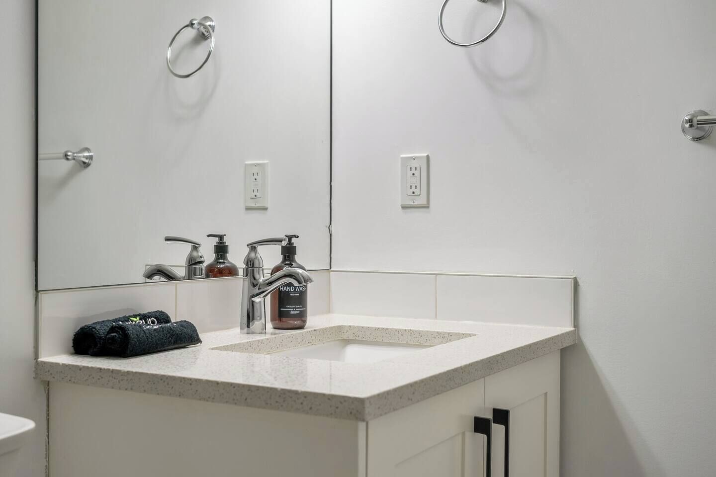 A modern bathroom with a white sink, two faucets, a mirror, and a towel.