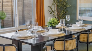 A dining table set with white plates, bowls, and wine glasses, surrounded by wicker chairs.