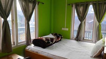 A room with a bed, a desk, and two windows with curtains.