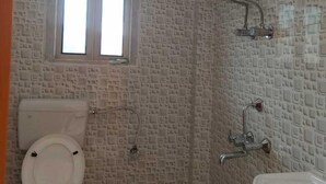 A small bathroom with a toilet, a window, a shower, and a sink.