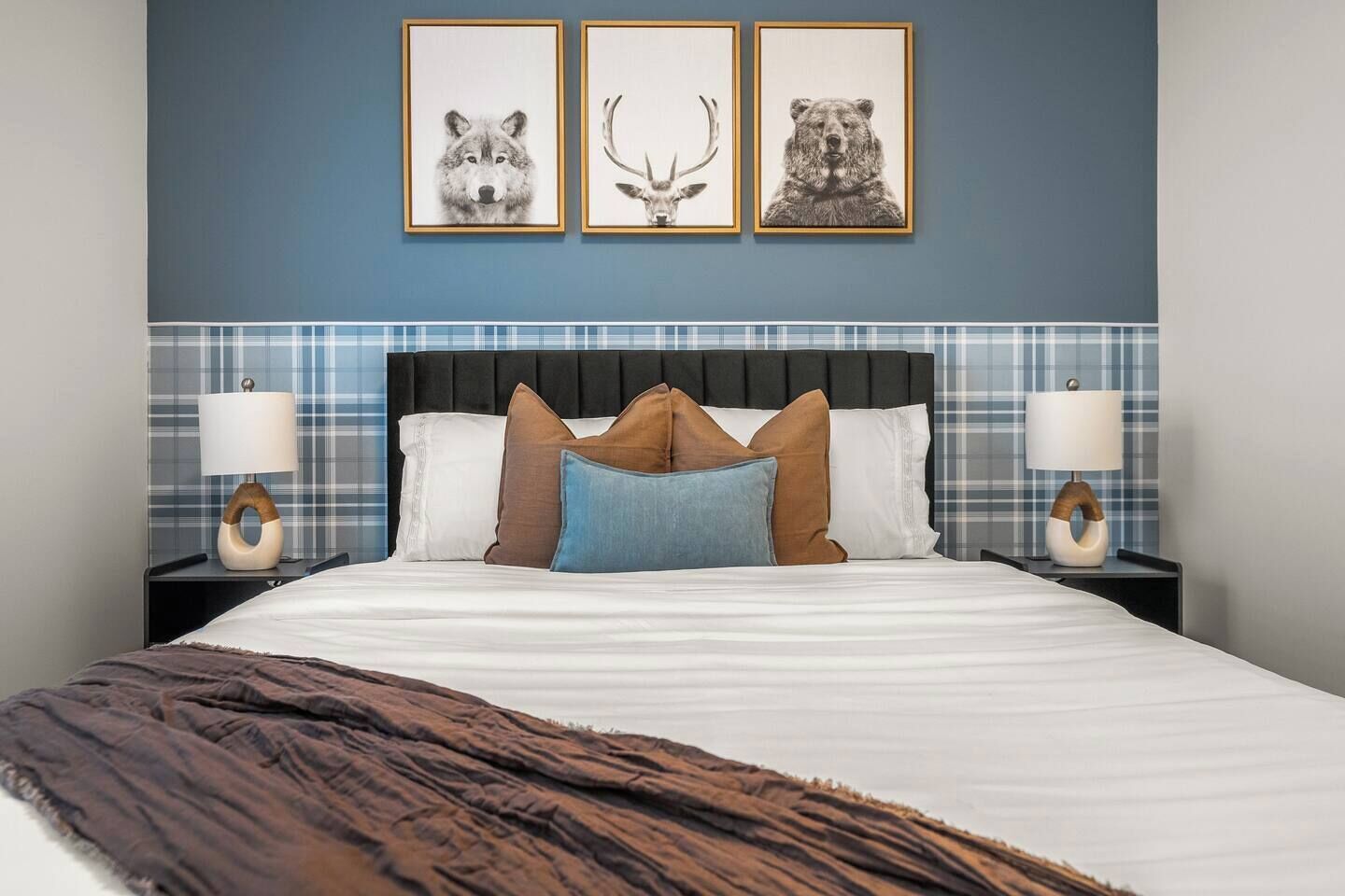 Un dormitorio con cama, almohadas, una colcha y cuadros con imágenes de un lobo, un ciervo y un oso.