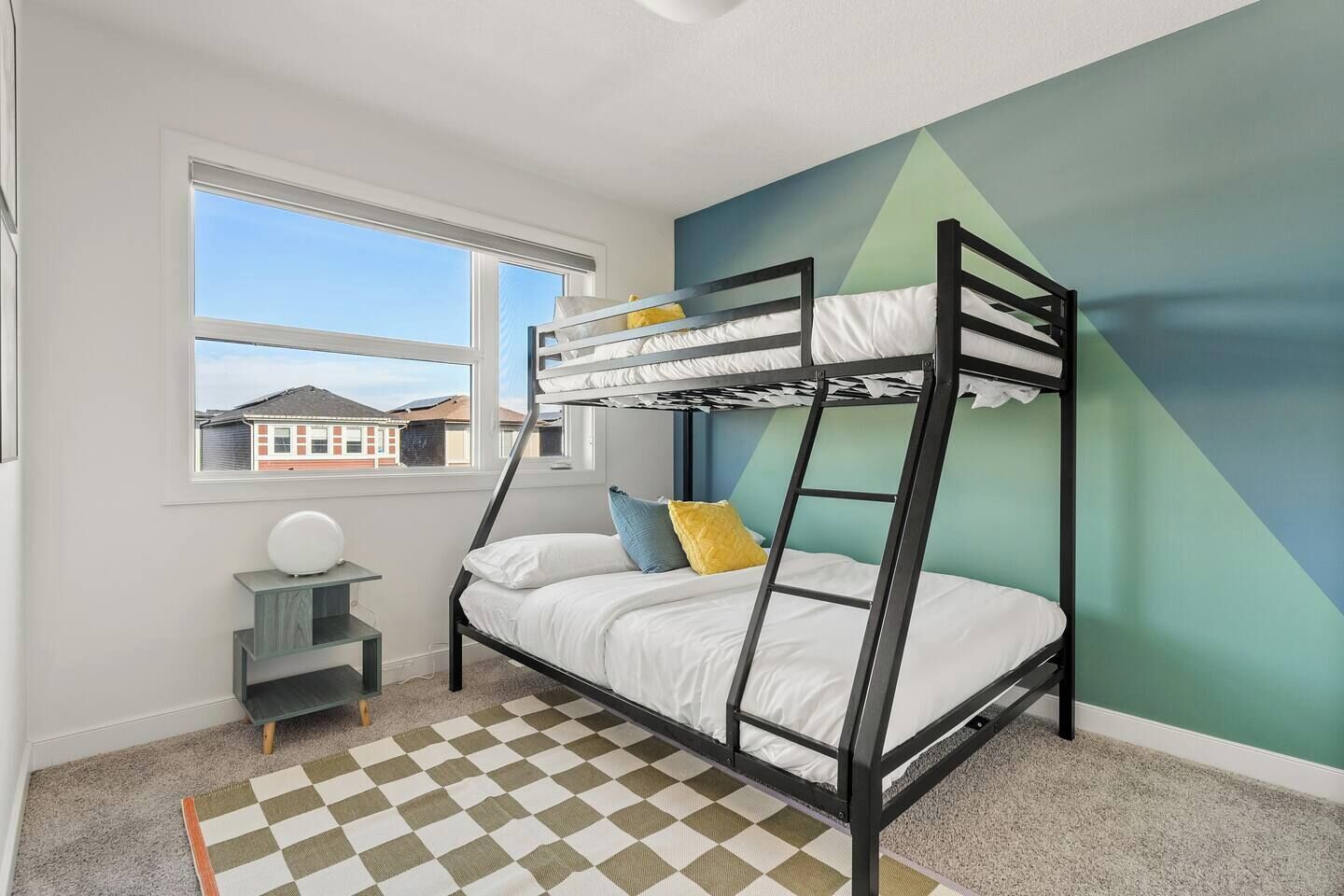 Une chambre avec un lit superposé, une fenêtre, un tapis à carreaux et un motif géométrique sur le mur.