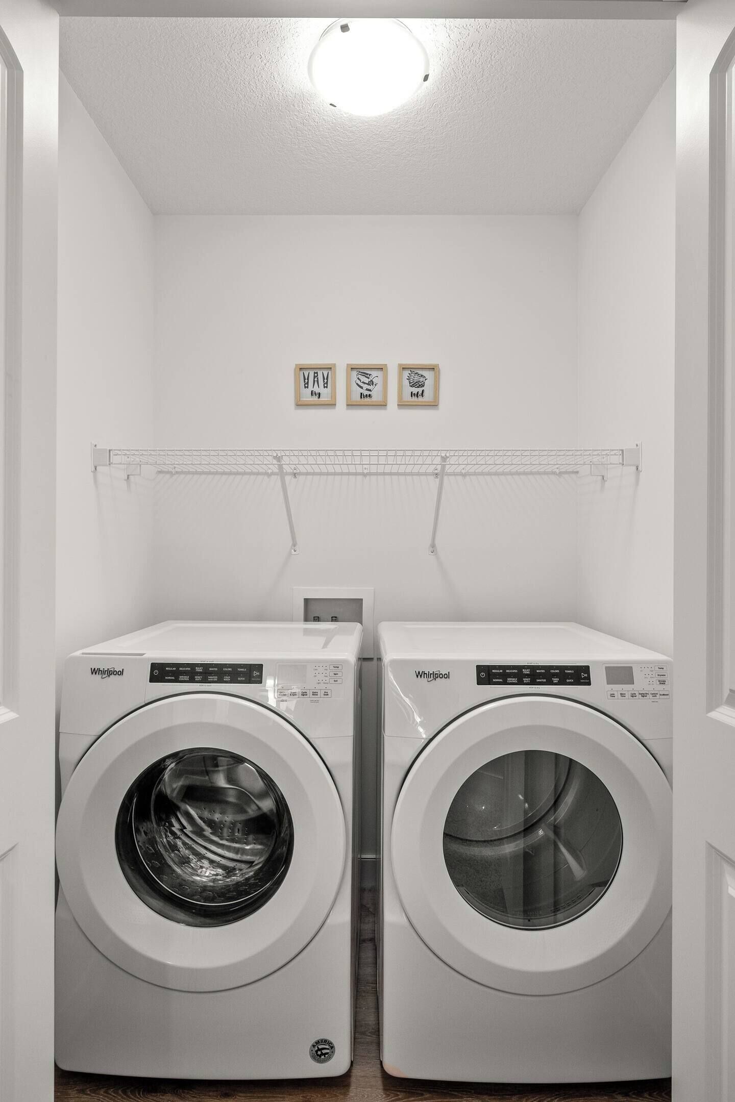 Uma lavanderia com duas máquinas de lavar Whirlpool de abertura frontal, um escorredor de metal e uma lâmpada no teto.