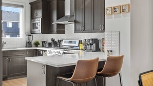 Een moderne keuken met donkere kasten, een groot schiereiland met krukken, een magnetron, fornuis en diverse apparaten.