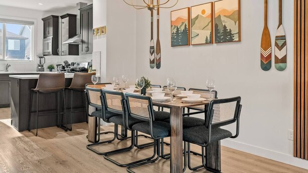 Een moderne keuken met donkere kastjes, een centraal eiland en een eethoek met een houten tafel en stoelen.