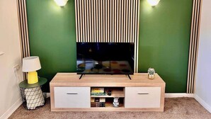 A TV on a wooden stand with a green wall and striped panels behind it. - A Vibrant 3-bedroom House With Ample Parking (Derby)