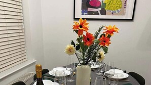A dining table set with white plates, glasses, and cutlery, a bottle of wine, and a vase with flowers. - A Vibrant 3-bedroom House With Ample Parking (Derby)