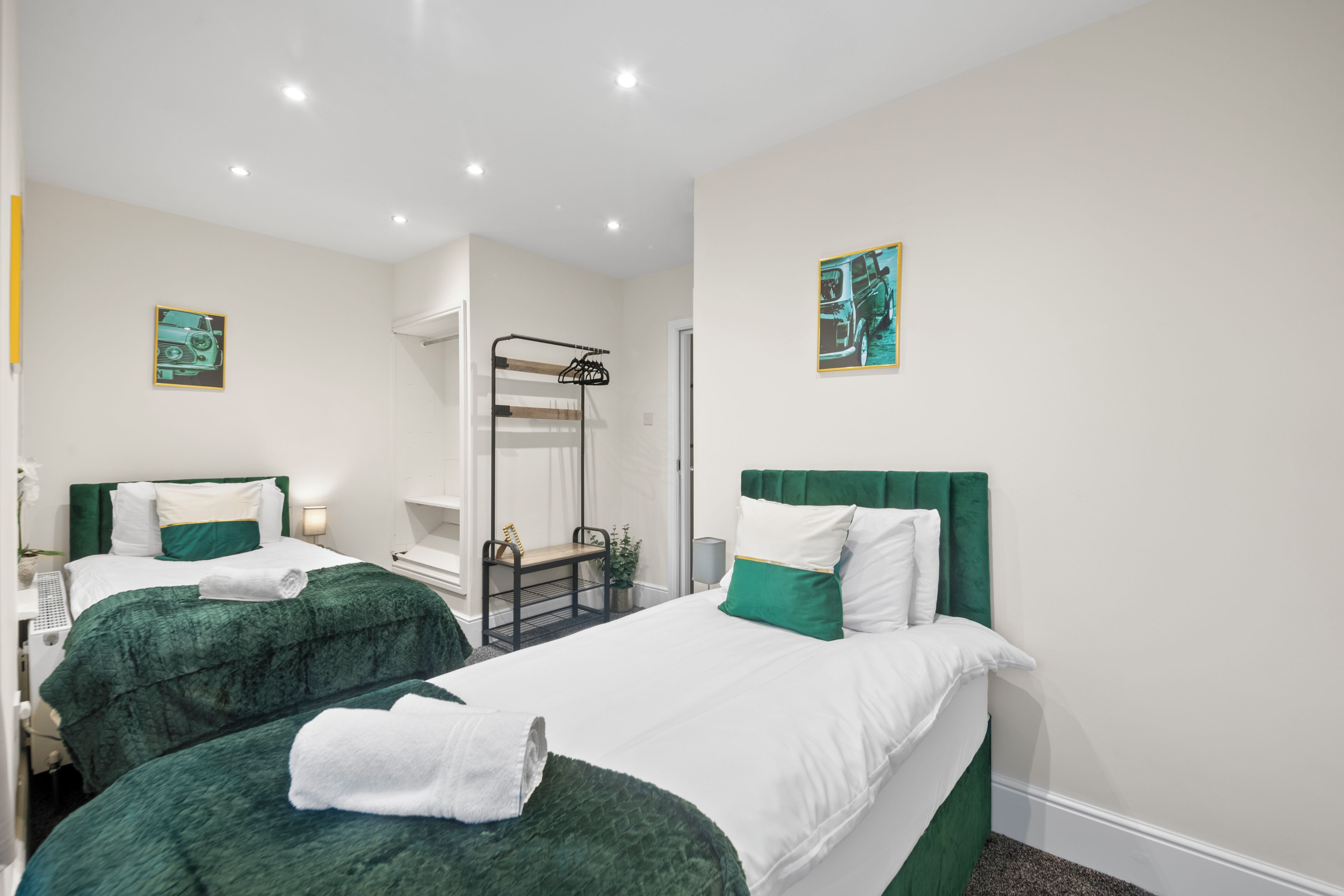 A hotel room with two beds, each with green and white bedding, a small seating area, and artwork on the walls.