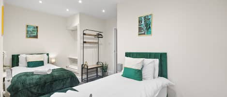 A hotel room with two beds, each with green and white bedding, a small seating area, and artwork on the walls.