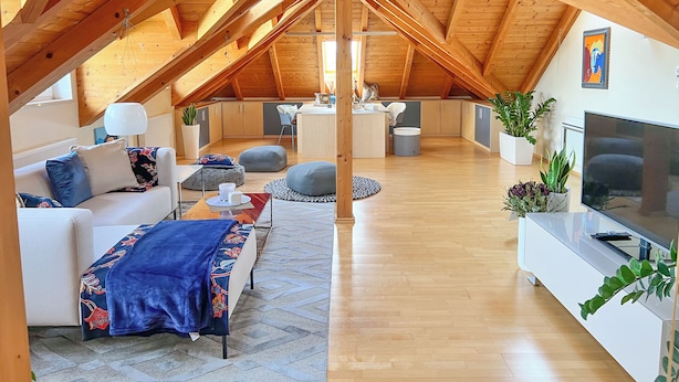 Une chambre mansardée avec un plafond en bois, un canapé, une télévision et un coin repas.