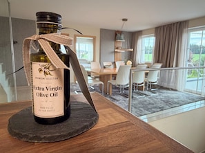 A bottle of Extra Virgin Olive Oil on a slate coaster in a modern dining area with a view of a balcony.