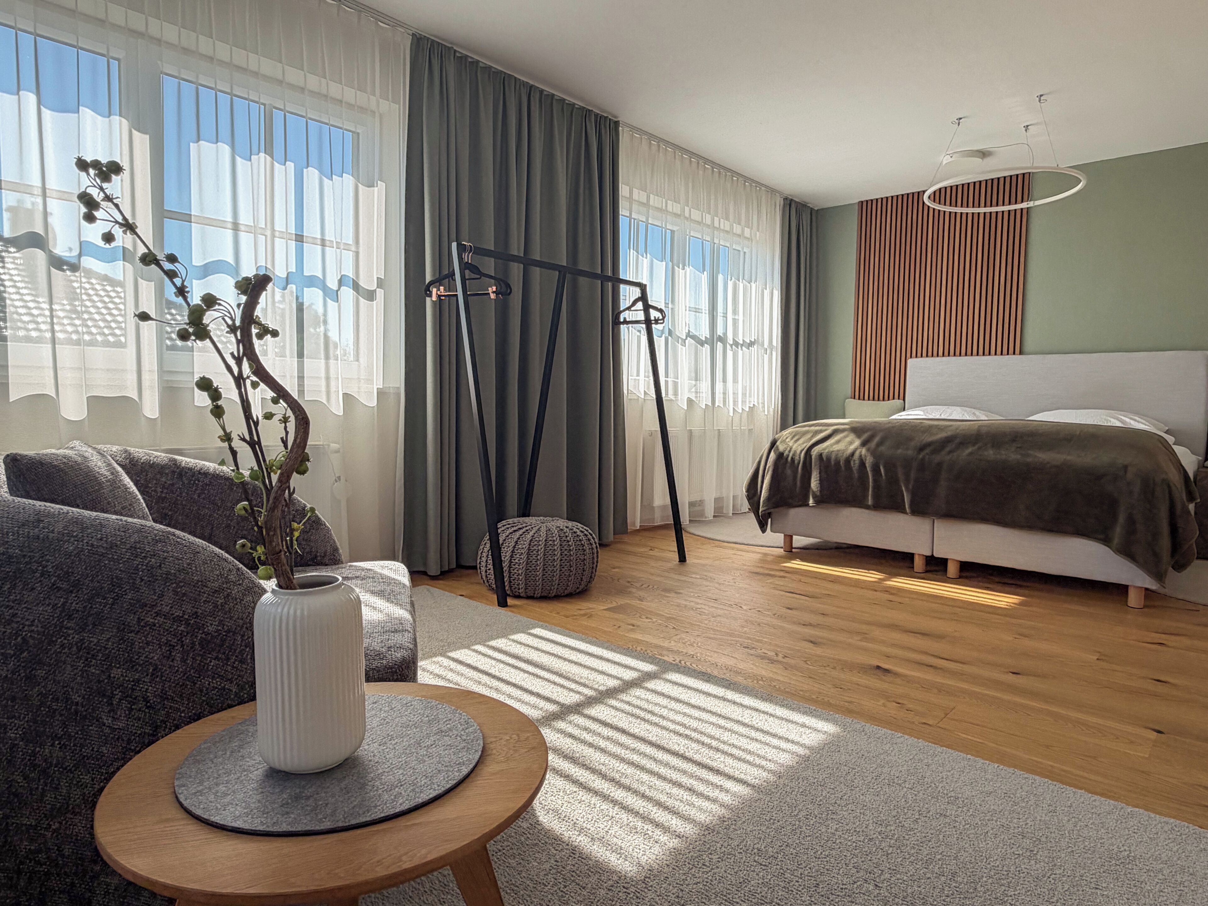 Ein modernes Schlafzimmer mit einem Bett, einer Sitzecke mit Tisch und einem fenster mit Vorhängen.