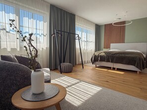 A modern bedroom with a bed, a seating area with a table, and a window with curtains.