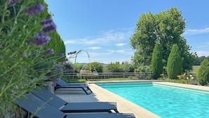 Une piscine entourée de verdure et d’arbres, avec des chaises longues et un fauteuil suspendu.