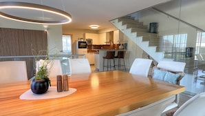 Une cuisine moderne dotée d’un îlot central, d’un coin repas avec une table en bois et d’un escalier menant à un niveau supérieur.