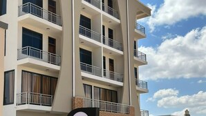 Un hotel de varios pisos con balcones, un cartel con el nombre Glonency M. Hotel, y una entrada con portón.