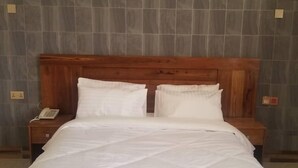 Una cama bien hecha con sábanas blancas, un cabecero de madera y un cuadro de un atardecer sobre ella.
