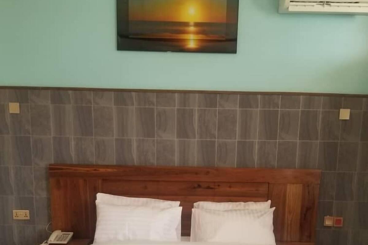 Una cama bien hecha con sábanas blancas, un cabecero de madera y un cuadro de un atardecer sobre ella.