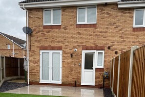 A two-story brick house with white-framed windows and doors, a satellite dish, and a small garden area with a wooden fence. - Sheffield Blissful Retreat - 3 Bedroom House (Sheffield)