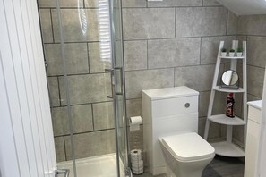 A modern bathroom with a glass shower enclosure, a toilet, and a shelf with toiletries. - Sheffield Blissful Retreat - 3 Bedroom House (Sheffield)