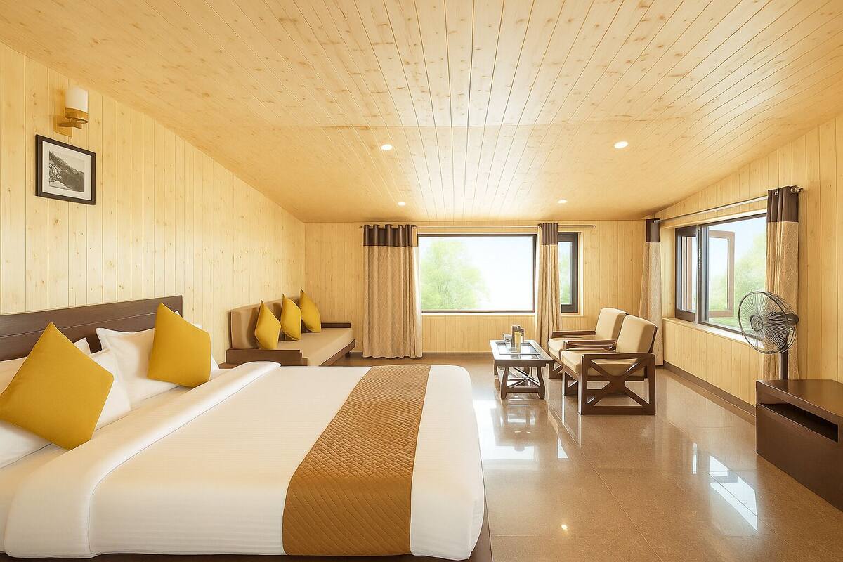 A hotel room with a wooden ceiling, a large bed with white and yellow bedding, a sofa, a table, and a chair.