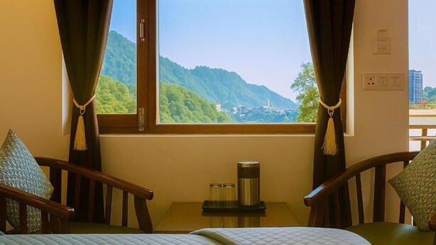A room with a bed, two chairs, a small table with a kettle, and a window offering a view of green hills. - Hotel Sunny Cot - Free Mall shuttle and Parking (Dehradun)