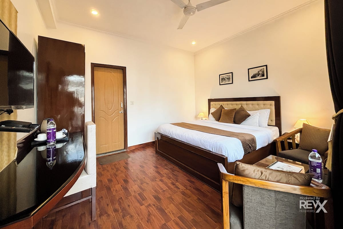A hotel room with a bed, bedside table, chair, desk, and a ceiling fan.