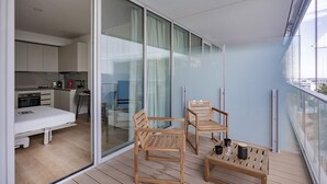 A balcony with wooden furniture, a bed, and a kitchen area visible through glass doors. - Waterfront Vibes by Wonderful Italy (Genoa)