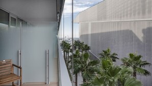 A balcony with a wooden bench, a glass door, and a view of palm trees and a building. - Waterfront Vibes by Wonderful Italy (Genoa)