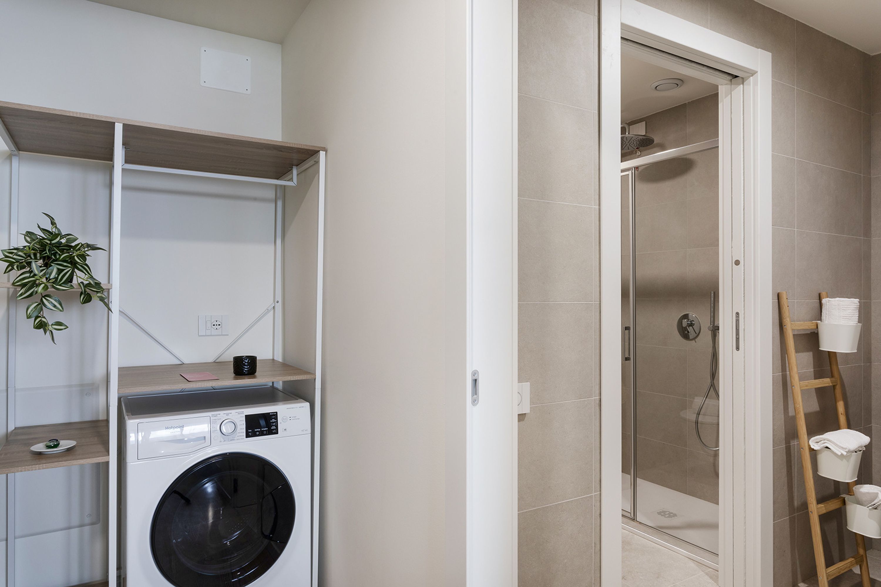 A laundry area with a washing machine, a shelf with a plant, and a shower area with a ladder.
