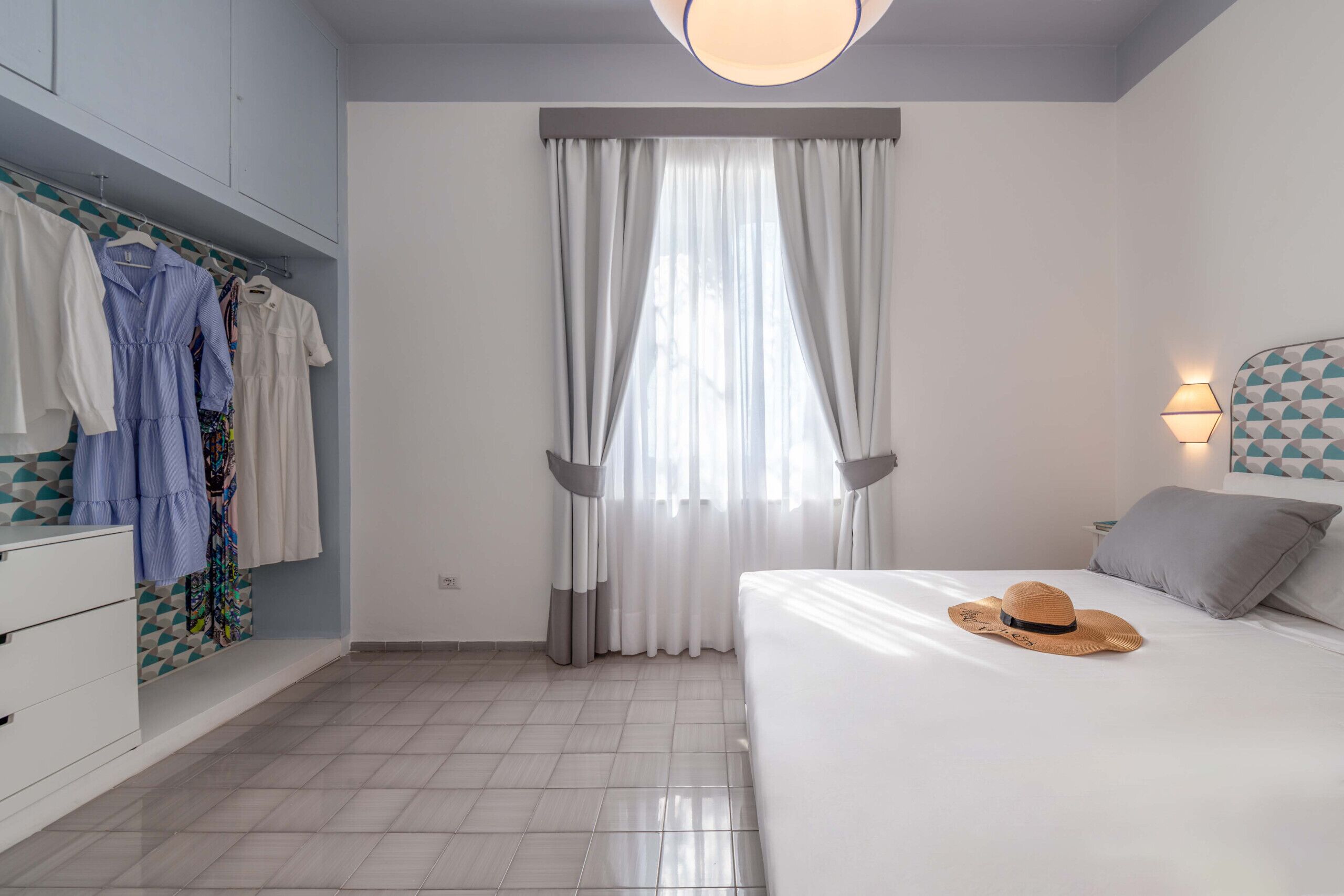 A bedroom with a bed, a wardrobe, a hanging clothes rack, and a window with curtains.