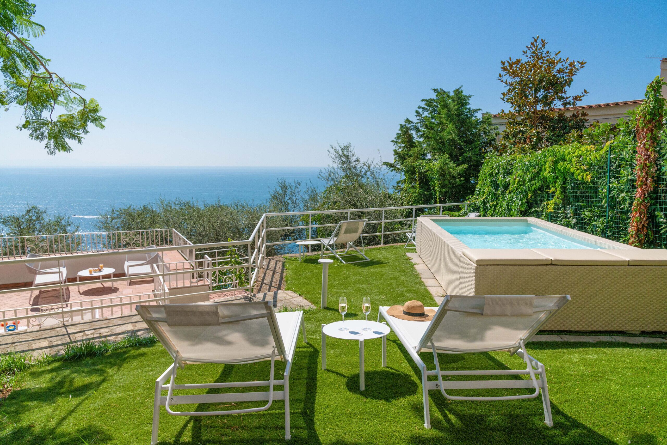 Uma área à beira da piscina com vista para o mar, uma banheira de hidromassagem e mobiliário para o exterior.