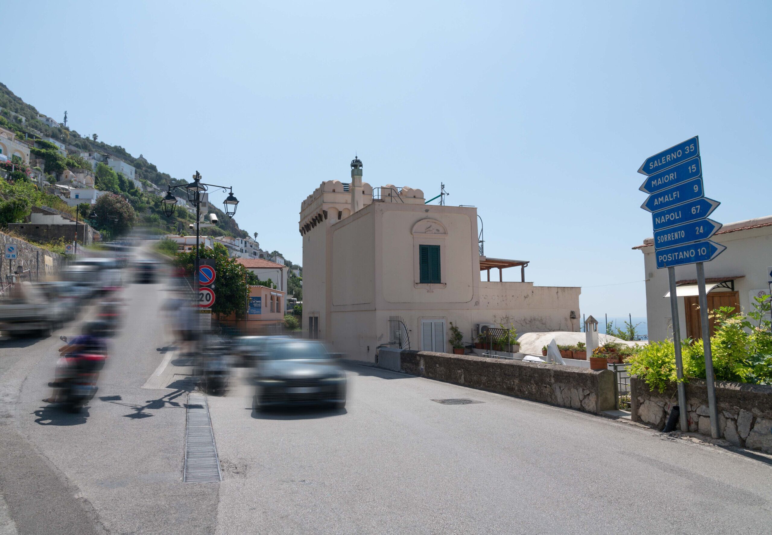 A street with a building that has a clock tower and a signpost with directions to various destinations.
