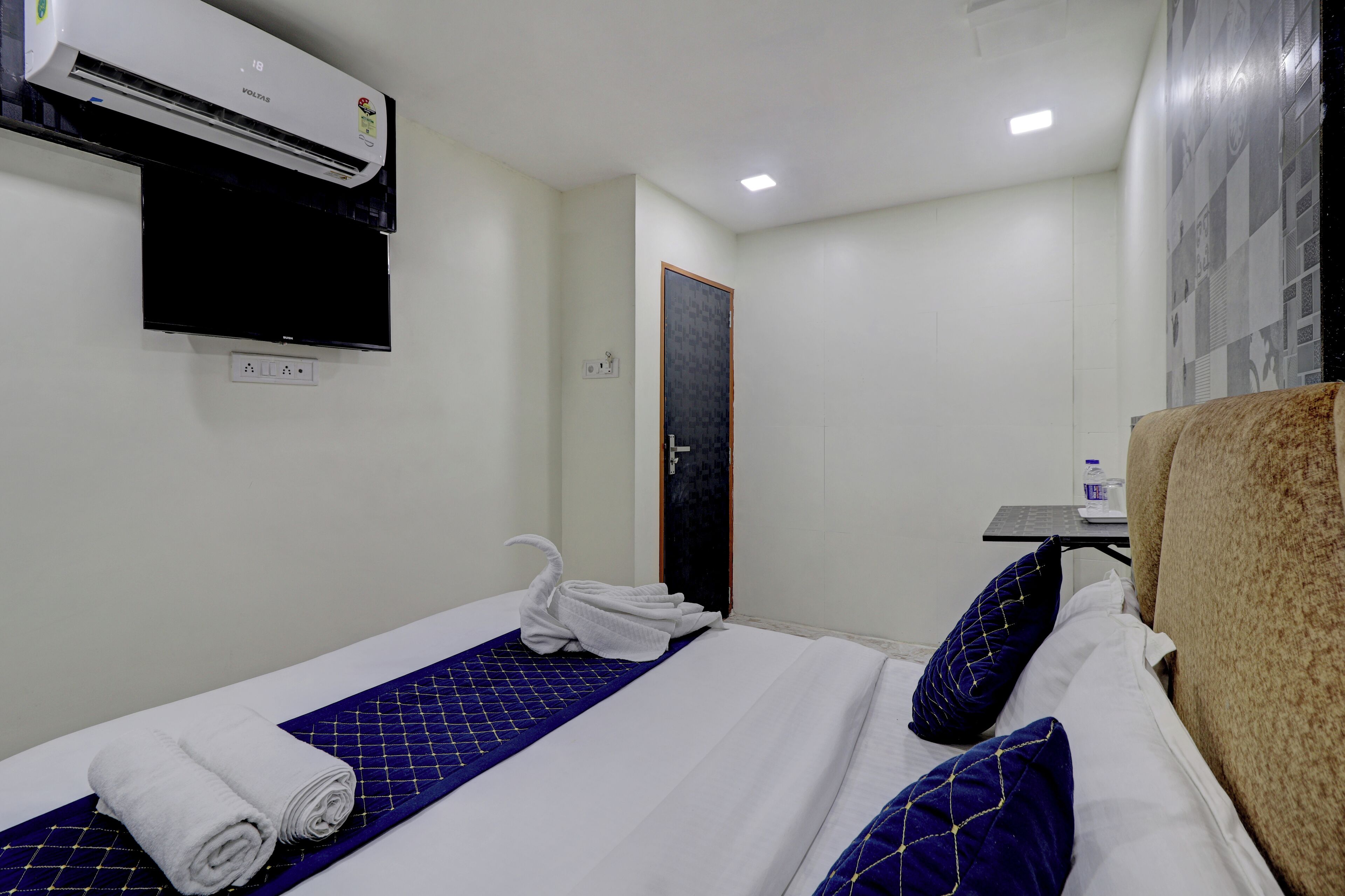 Habitación de hotel con cama, televisión de pantalla plana montada en la pared, unidad de aire acondicionado y puerta que da a otra habitación.