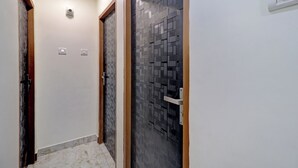 A hallway with two doors, one with a patterned glass door and the other with a wooden frame. There are light switches on the wall and a smoke detector on the ceiling. - Parle Inn Hotel (Mumbai)