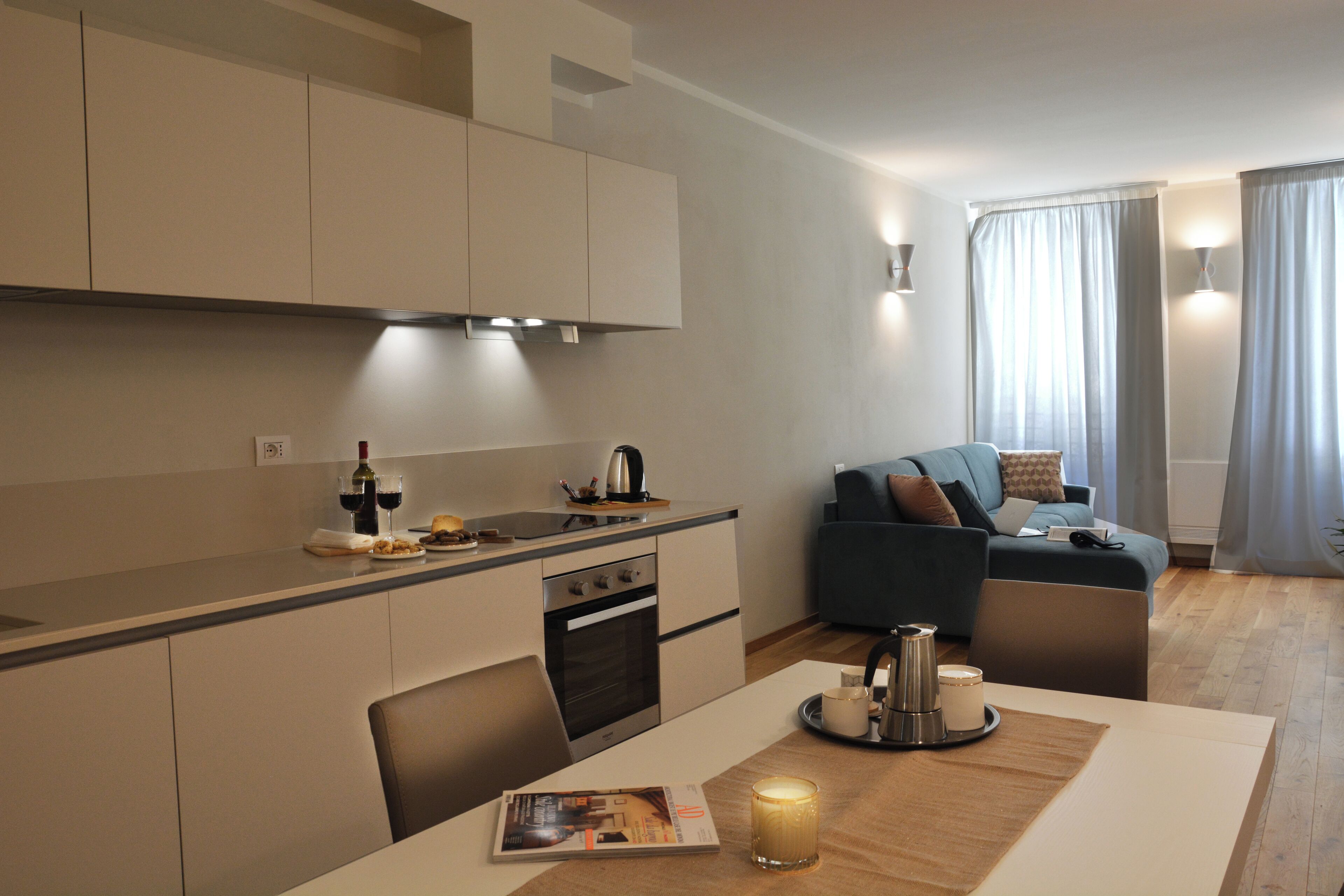 A modern kitchen with a dining area, a sofa, and a table with a magazine and candle.