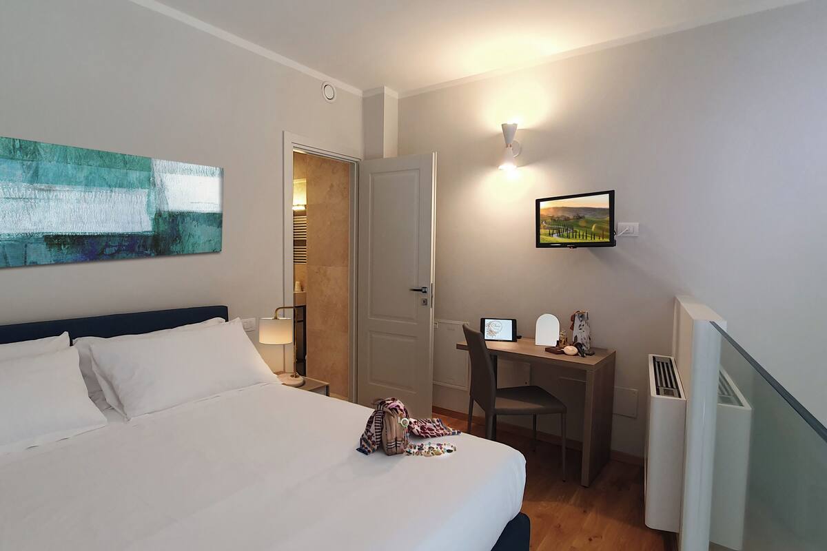 A hotel room with a bed, a desk, a chair, a TV, and a painting on the wall.