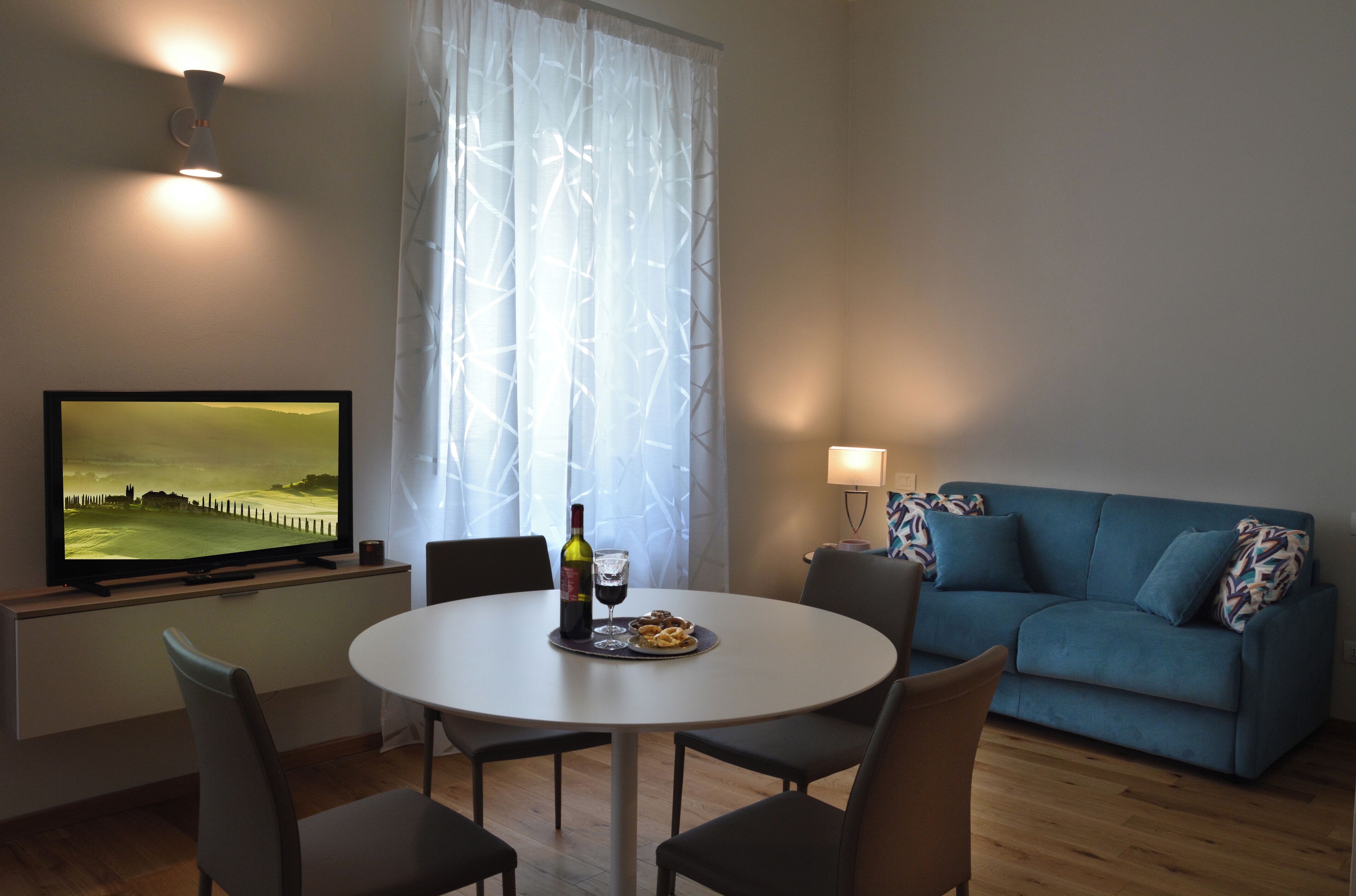 A living room with a TV, a dining table with chairs, a sofa, and a lamp.