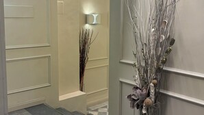 A hallway with a light fixture, a decorative wall piece, and a vase with branches.