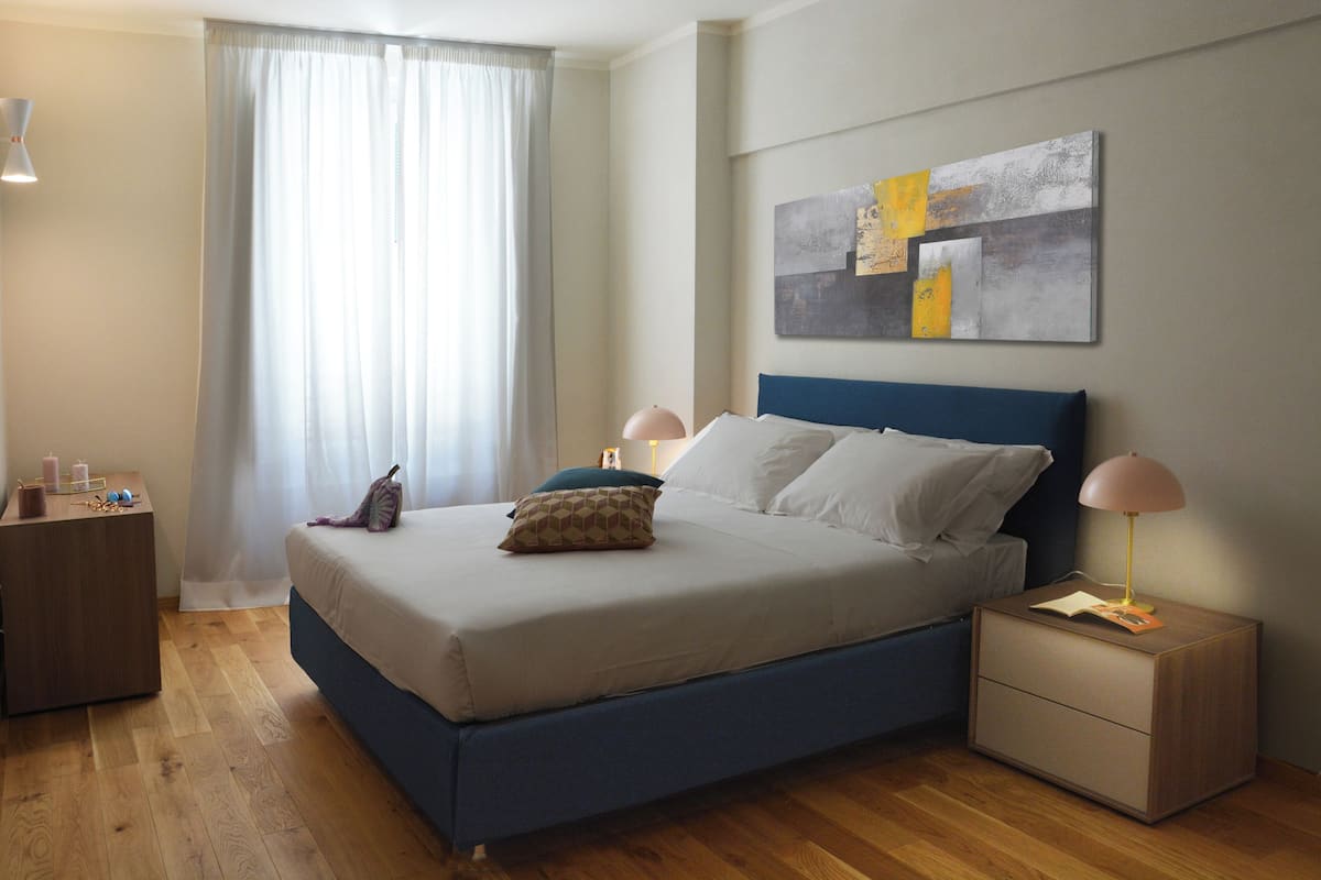 A modern bedroom with a large bed, bedside tables, and a wall art piece.