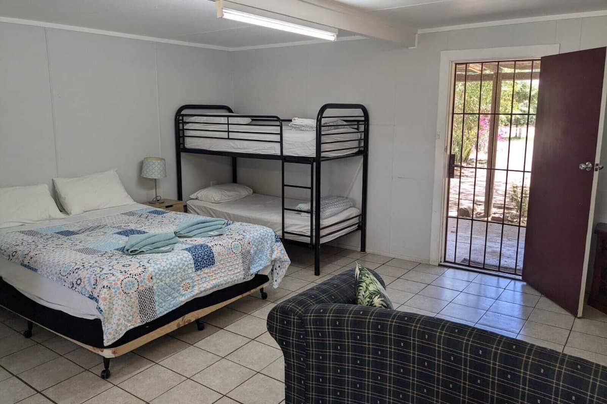 Une pièce comprenant un lit, un lit superposé, une chaise et une porte donnant sur l’extérieur.