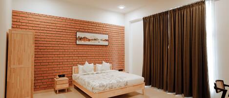 Une chambre avec un mur en briques, un lit, une armoire, un ventilateur de plafond et une fenêtre avec des rideaux.