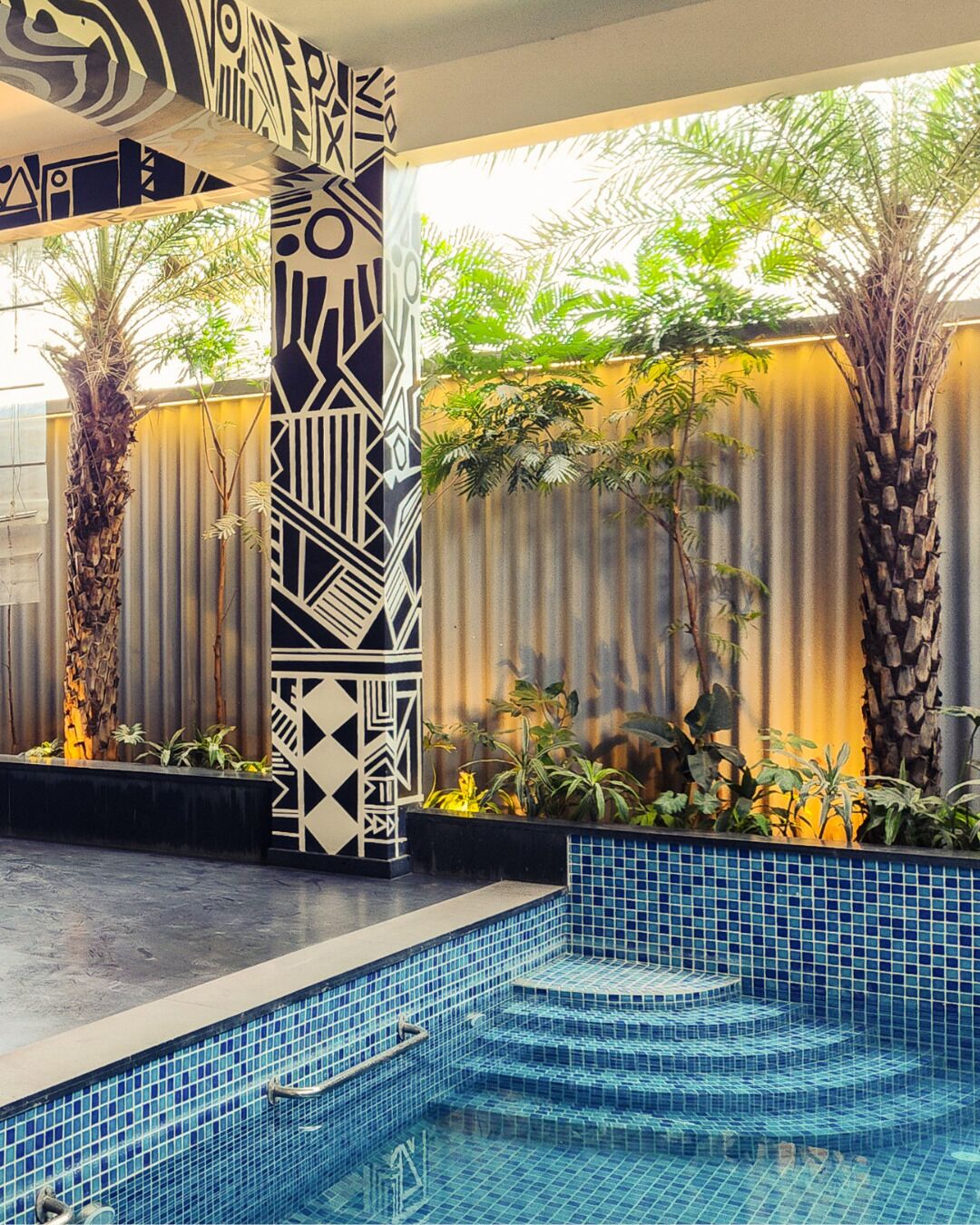 A pool area with geometric wall patterns, palm trees, and tiled flooring.