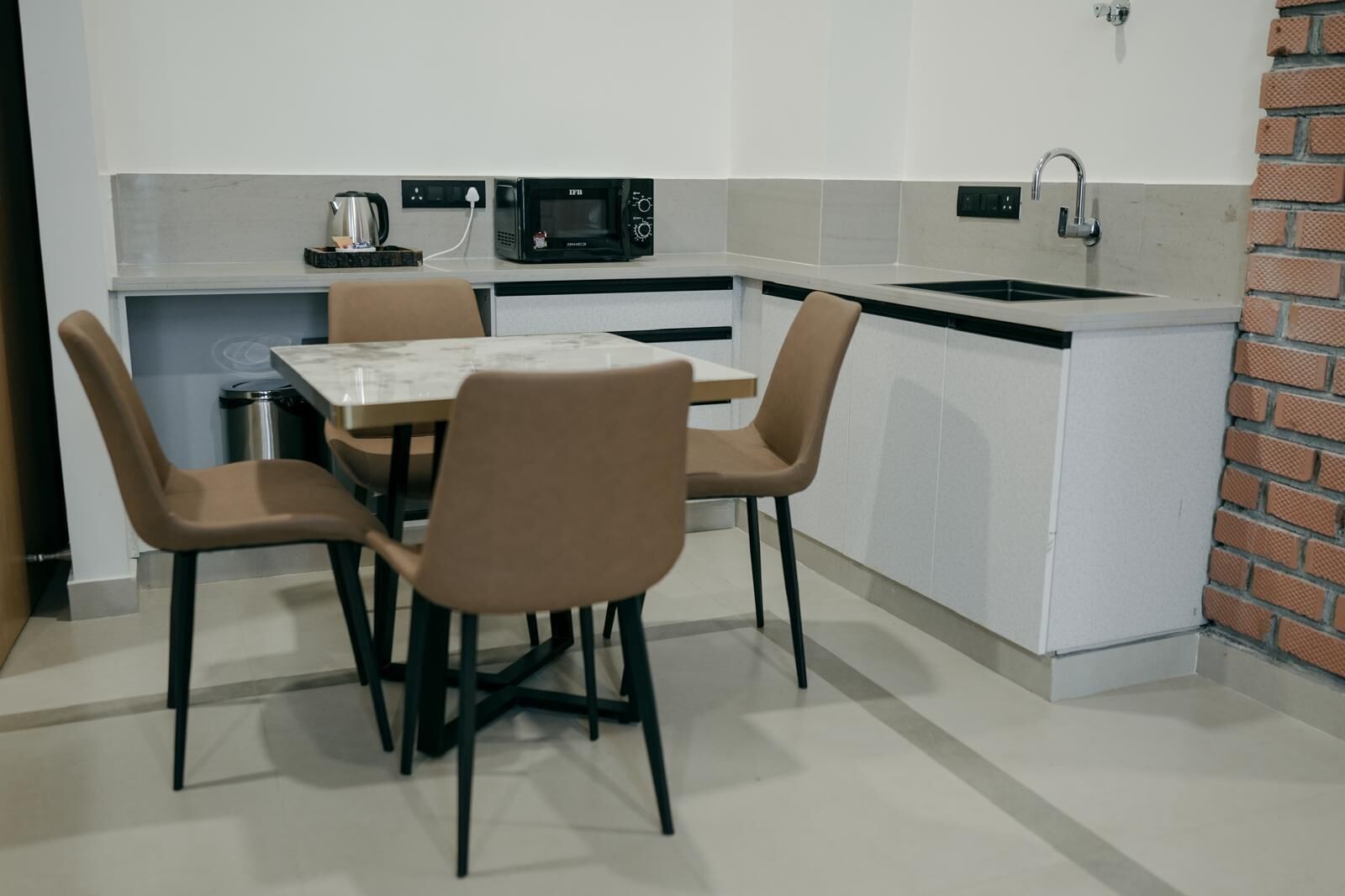 Una cocina compacta con una mesa de comedor y cuatro sillas, microondas, hervidor y un lavabo.