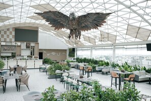Ένα ευρύχωρο εστιατόριο στην ταράτσα, με ψηλό ταβάνι, μεγάλα παράθυρα και ένα εντυπωσιακό γλυπτό που κρέμεται στο κέντρο.