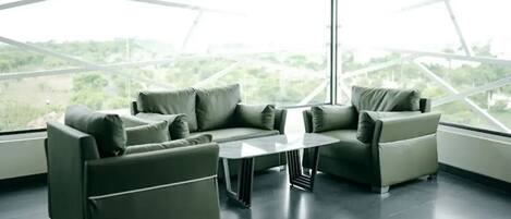 A modern room with a sectional sofa, a coffee table, and large windows offering a view of greenery.
