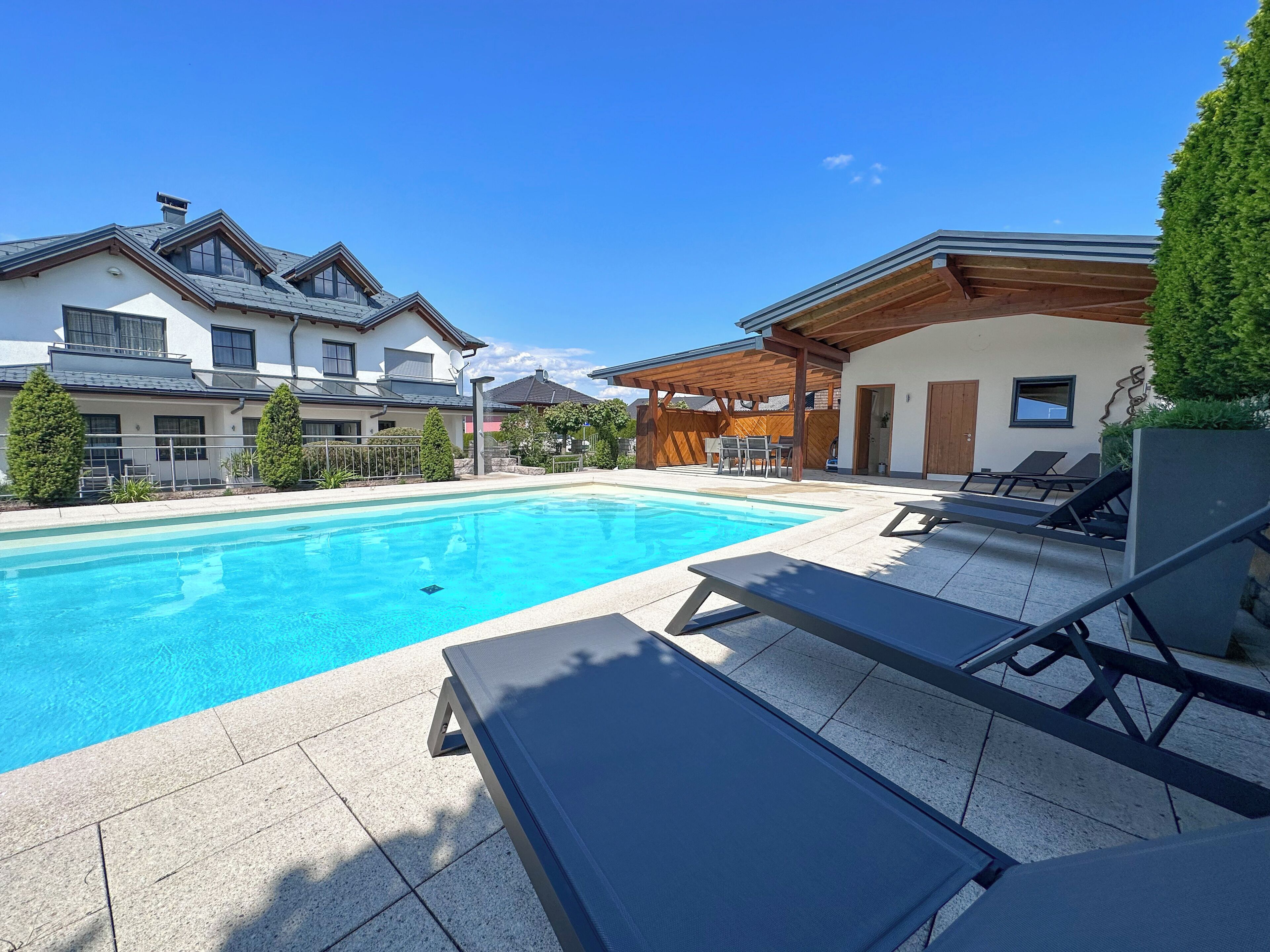 A swimming pool with lounge chairs, a wooden pergola, and a view of modern houses.