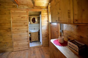 Interior de uma cabana de madeira, com porta de madeira que dá para o banheiro, uma pia e uma caixa de armazenamento à direita.