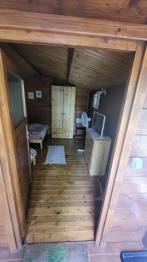 Um pequeno quarto de madeira com uma cama, cômoda, ventilador e televisão.