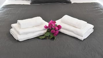 Uma cama bem arrumada com um cobre-leito cinza escuro, almofadas brancas e toalhas brancas dobradas dispostas simetricamente sobre a cama.